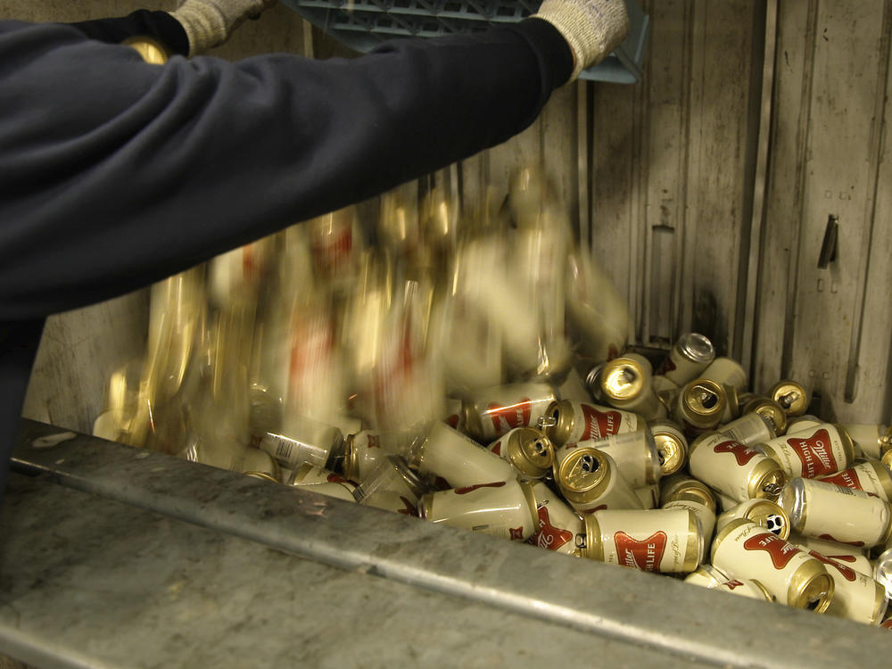 A worker dumps empty cans of Miller High Life beer into a machine to be crushed at the Westlandia plant in Ypres, Belgium, on Monday.