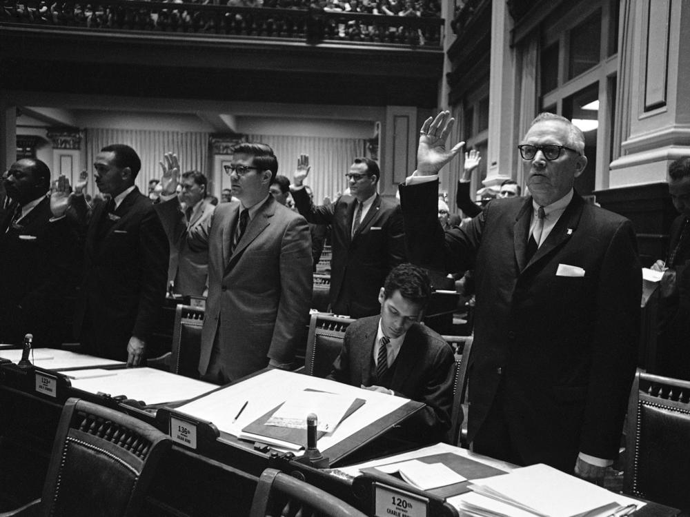 Rep.-elect Julian Bond, center, who was refused a seat in the Georgia House, looks through his desk as two of his Fulton County colleagues, Reps. Jack Etheridge, left, and Charlie Brown raise their hands for the oath of office in Atlanta, Jan. 10, 1966.