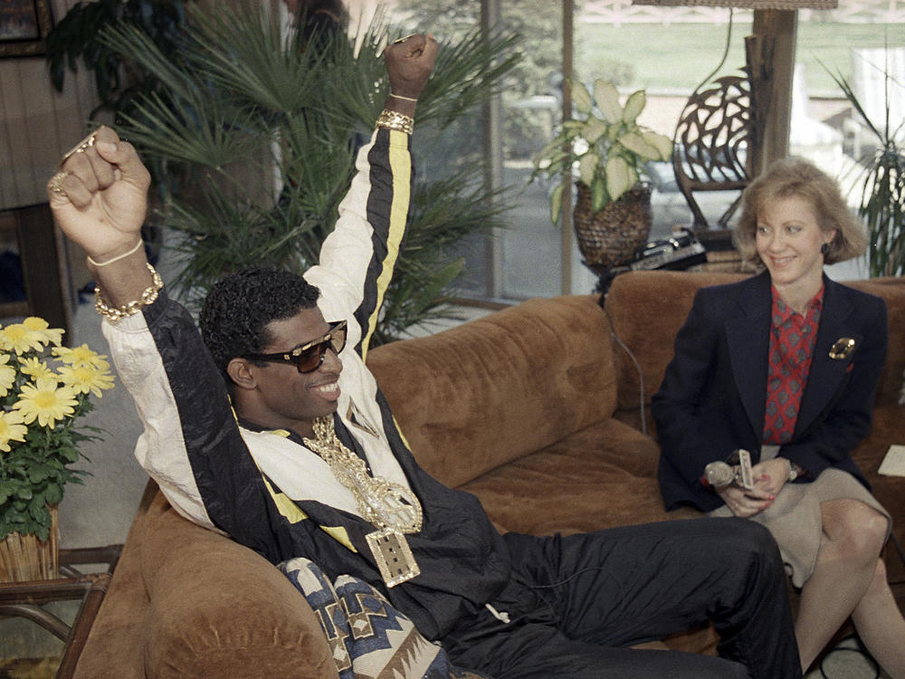Deion Sanders, left, reacts as he sits with television reporter Andrea Kremer, at his agent's suburban home in Winnetka, Ill., April 23, 1989. Sanders was selected by the Atlanta Falcons in the first round of the NFL draft. Sanders became the NFL draft's first fashion icon by accessorizing a black and white track suit with a loads of sparkling gold jewelry and dark shades.