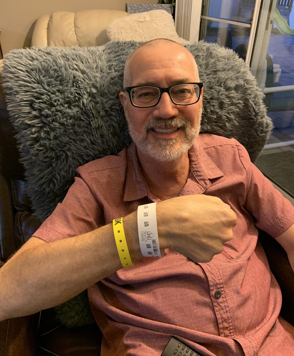 David Elder flashes his hospital bracelet from the comfort of an easy chair in his own home, which he was sent back to just a few hours after his bone marrow transplant surgery. He said it was a lot more restful to be home.