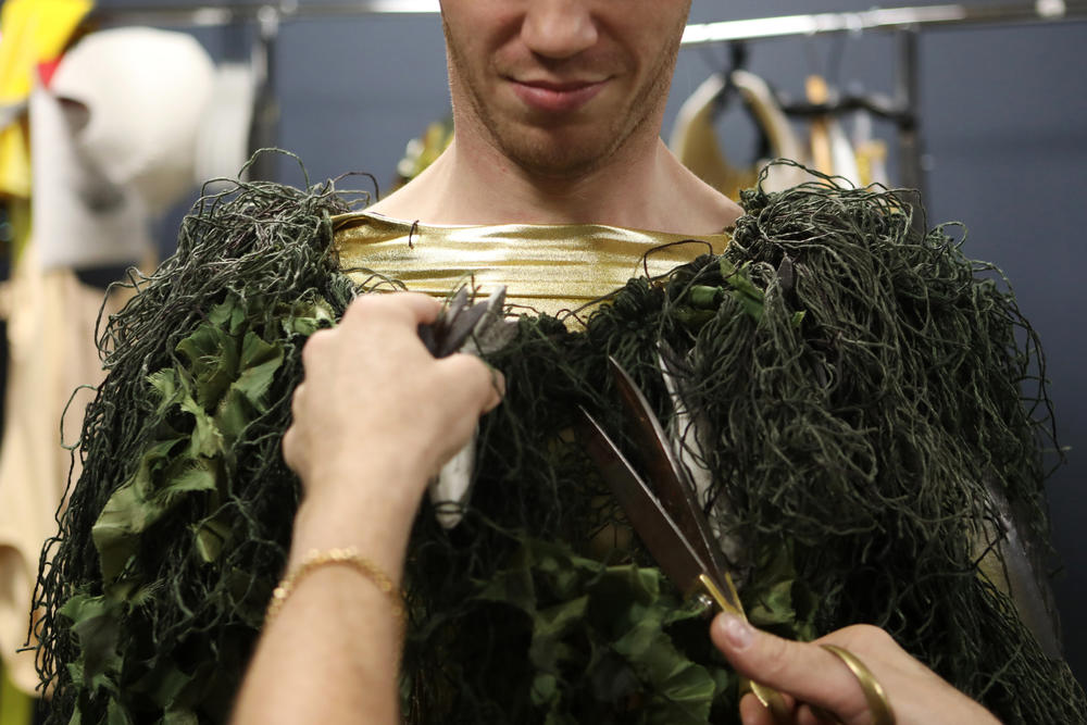 Machine Dazzle removes excess pieces of a costume of Apollo disguised as a mortal – covered in synthetic algae, fishing net and fish – to try to seduce the opera's titular nymph Io.