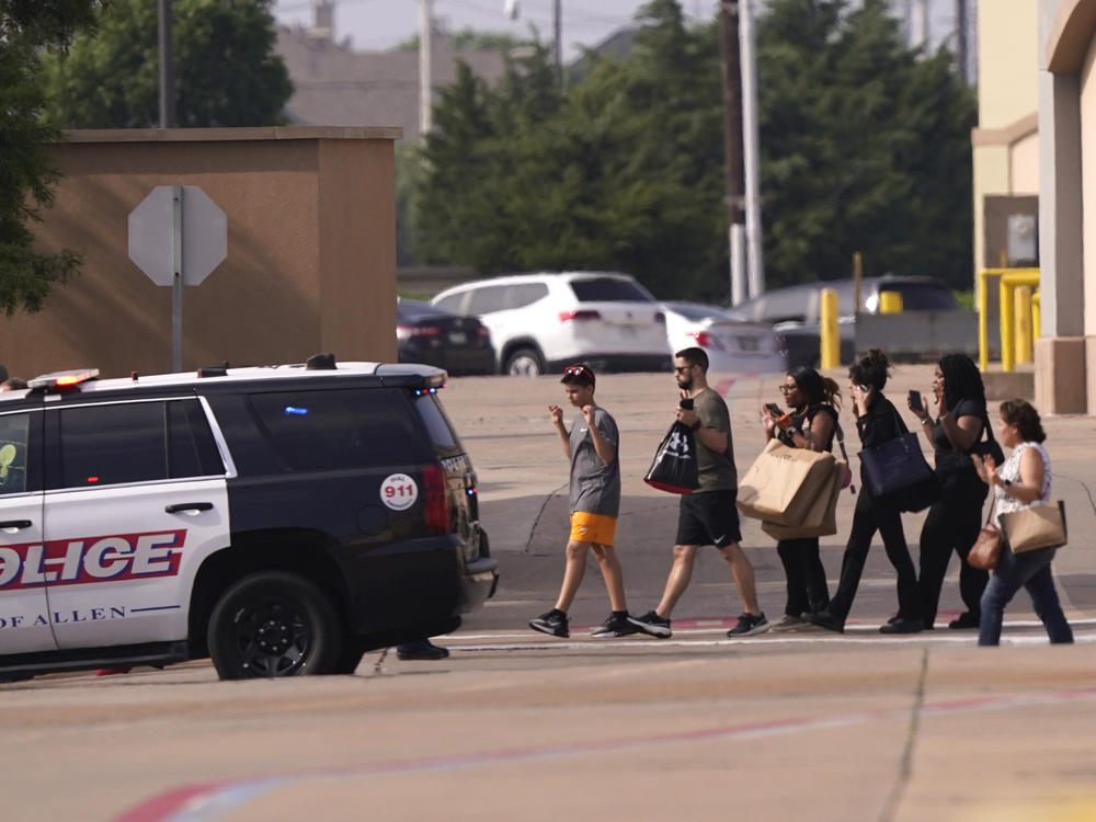 People raise their hands as they leave a shopping center following reports of a shooting, in Allen, Texas, on Saturday.