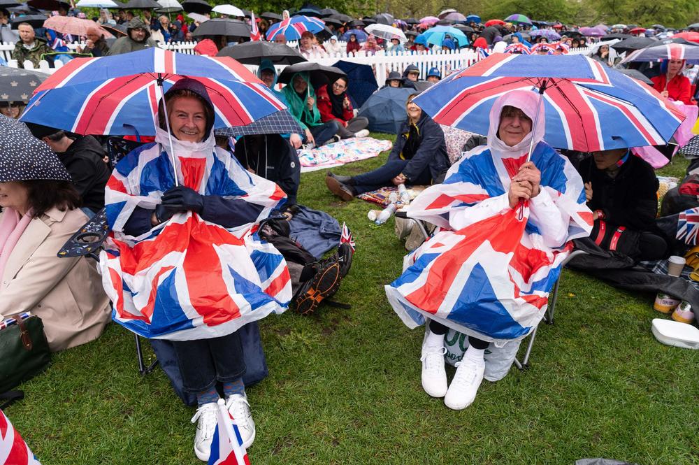 Well-wishers protect themselves against the rain as they wait along the route of the 'King's Procession'.