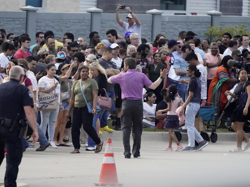 People gather across the street from a shopping center after the shooting on Saturday in Allen, Texas.