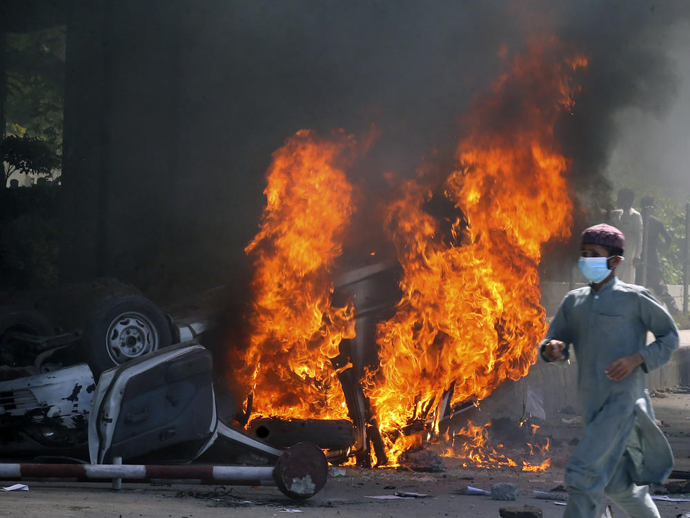 A man runs past a burning car set on fire by angry supporters of Pakistan's former Prime Minister Imran Khan during a protest against the arrest of their leader, in Peshawar, Pakistan, Wednesday. A court has ruled that former Pakistani Prime Minister Imran Khan can be held for questioning for eight days. His detention set off clashes between his supporters and police Tuesday.