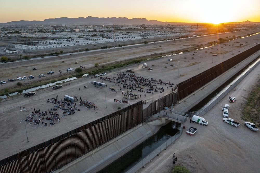 As the sun sets, migrants wait outside a gate in the border fence to enter into El Paso, Texas, to be processed by the Border Patrol, on Thursday.