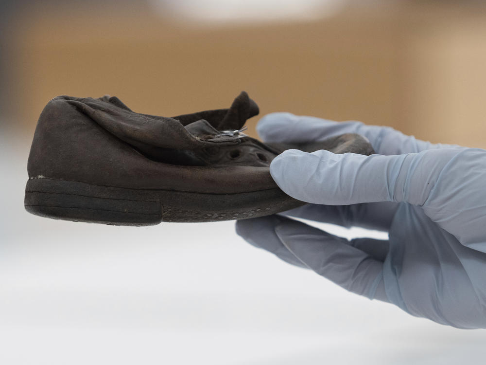 A worker holds a shoe that belonged to a child victim of the former Nazi German death camp Auschwitz-Birkenau at the conservation laboratory on the grounds of the camp in Oswiecim, Poland, Wednesday, May 10, 2023.