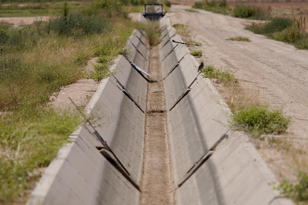 A dry irrigation canal runs between fields in Maricopa, Ariz., on Aug. 18, 2022.