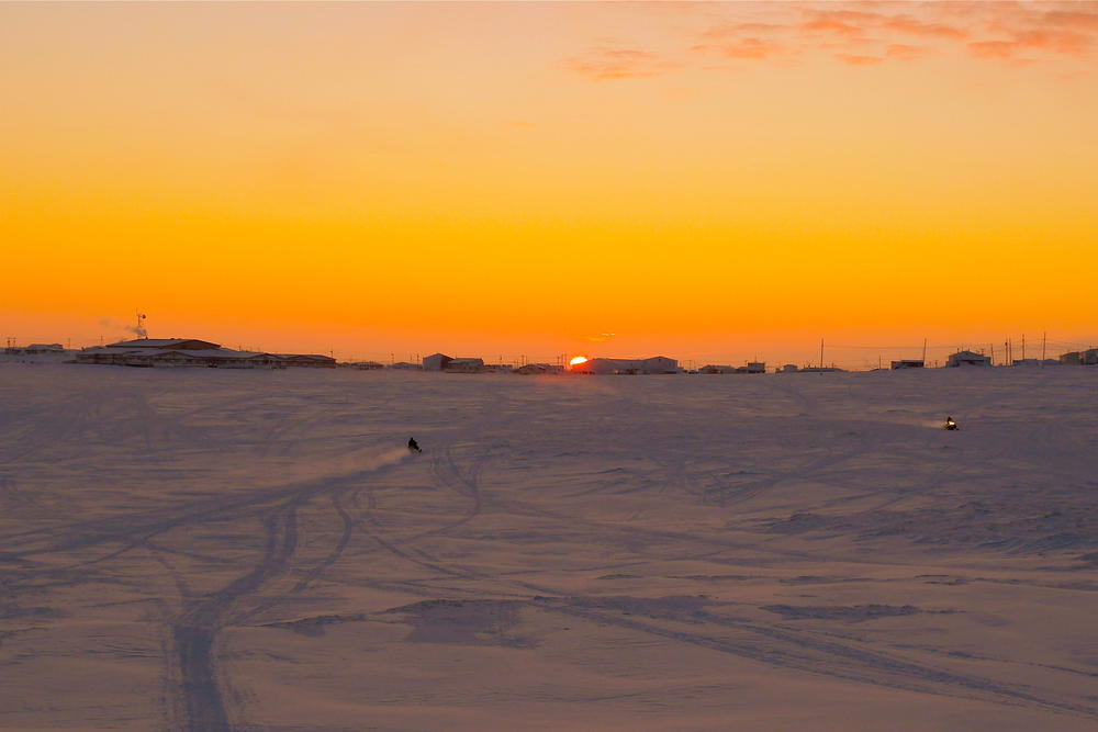 Snowmobiles glide across the tundra at sunset in Chevak.