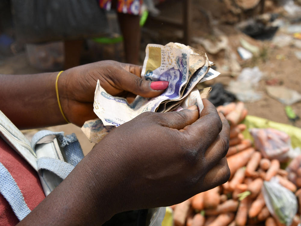 A vendor in a market in Nigeria counts local bills. The country is one of dozens whose devalued currency is fueling a debt crisis.
