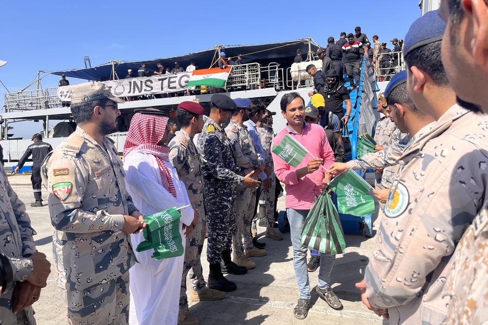 An Indian evacuee from Port Sudan disembarks from an Indian warship in Jeddah's main commercial port. Saudi officers stand ready to welcome evacuees from Sudan with Saudi flags. April 30, 2023.