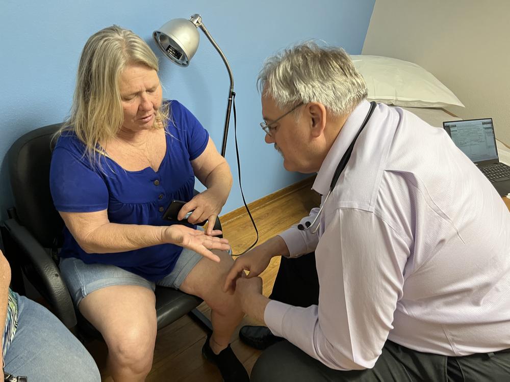 Alice Collins of Winterset, Iowa, shows osteopathic physician Kevin de Regnier a spot on her hand during an office visit on May 9, 2023. A surgeon recently removed a tumor from her hand.
