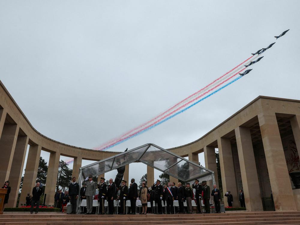 Guests, including U.S. Chairman of the Joint Chiefs of Staff Gen. Mark Milley and U.S. Secretary of Defense Lloyd Austin, watch as a French elite acrobatic flying team soars over Tuesday's ceremony at the Normandy American Cemetery and Memorial.