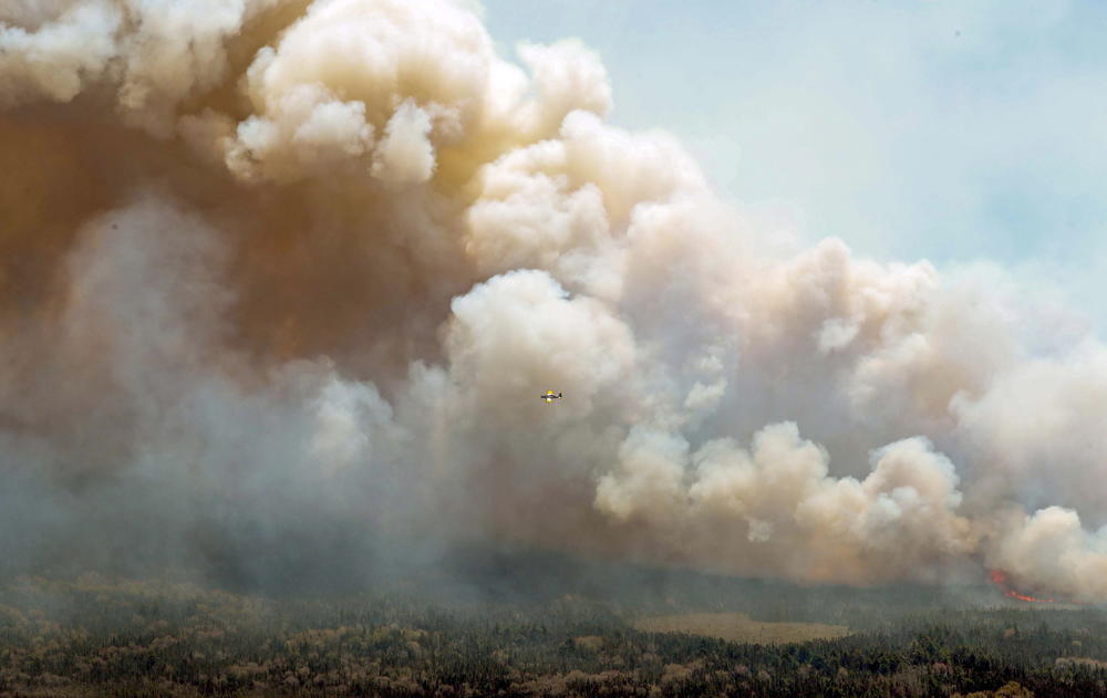 In this aerial image, an aircraft, center, flies near a wildfire burning near Barrington Lake in Shelburne County, Nova Scotia, on Wednesday, May 31, 2023.