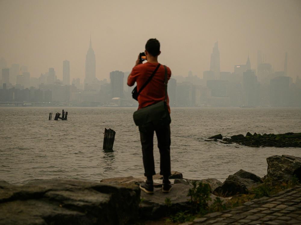 A man stands before the smoky New York City skyline and East River in Brooklyn on Tuesday.