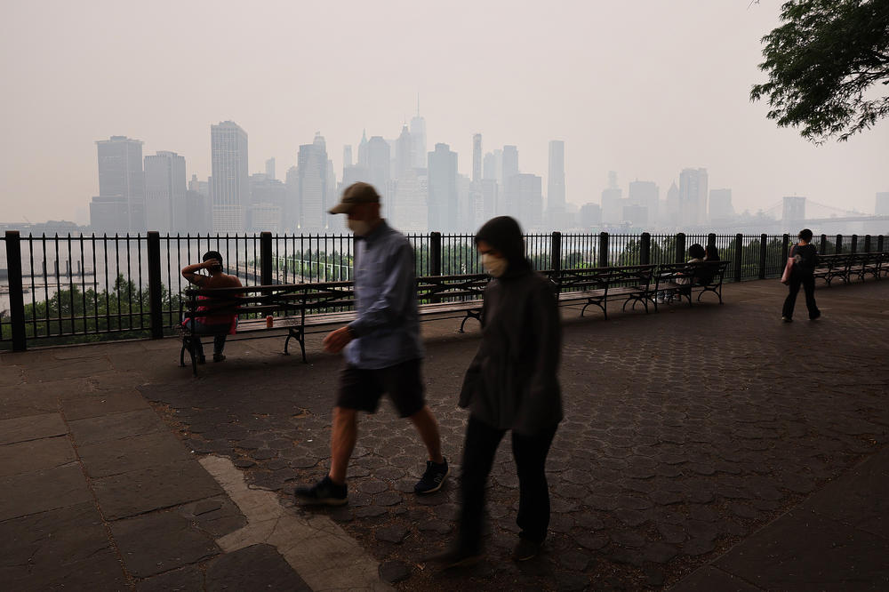 People walk along the Brooklyn Promenade as a reddish haze enshrouds the Manhattan skyline on Tuesday in New York City.