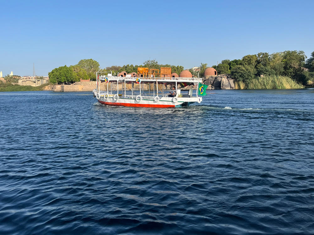 A small motorboat cruises down the Nile River in Aswan, Egypt, past domed Nubian structures.