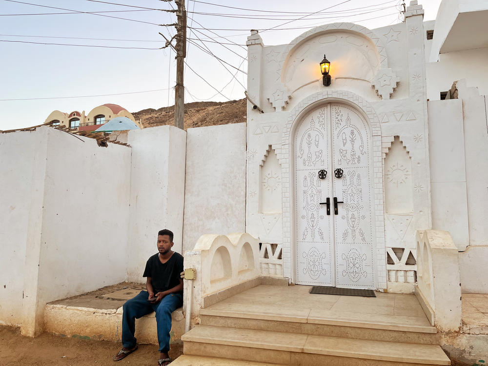 A man sits outside a building with a traditional Nubian domed entrance in Aswan, Egypt.