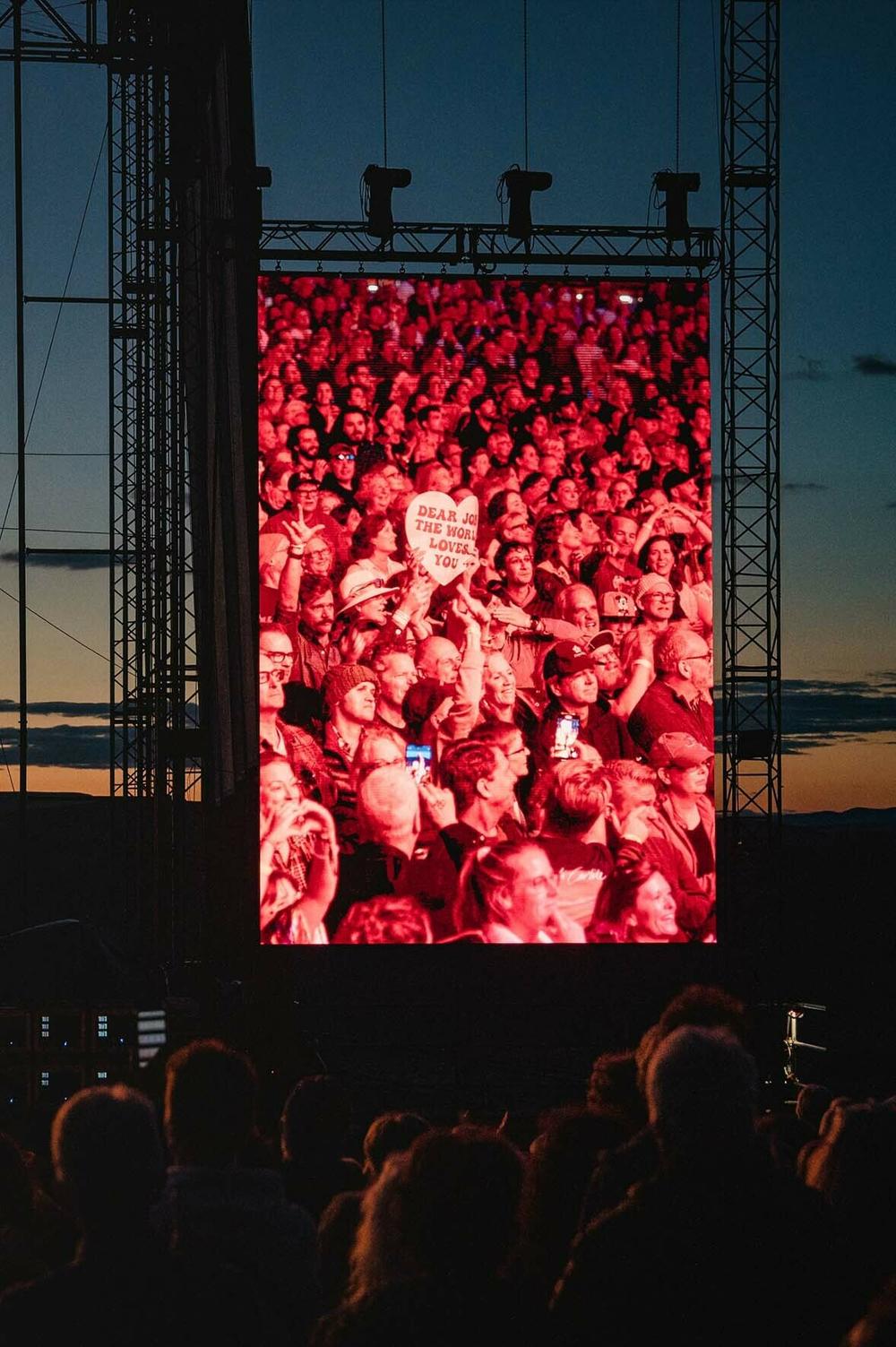 A member of the audience holds up a heart-shaped sign reading 