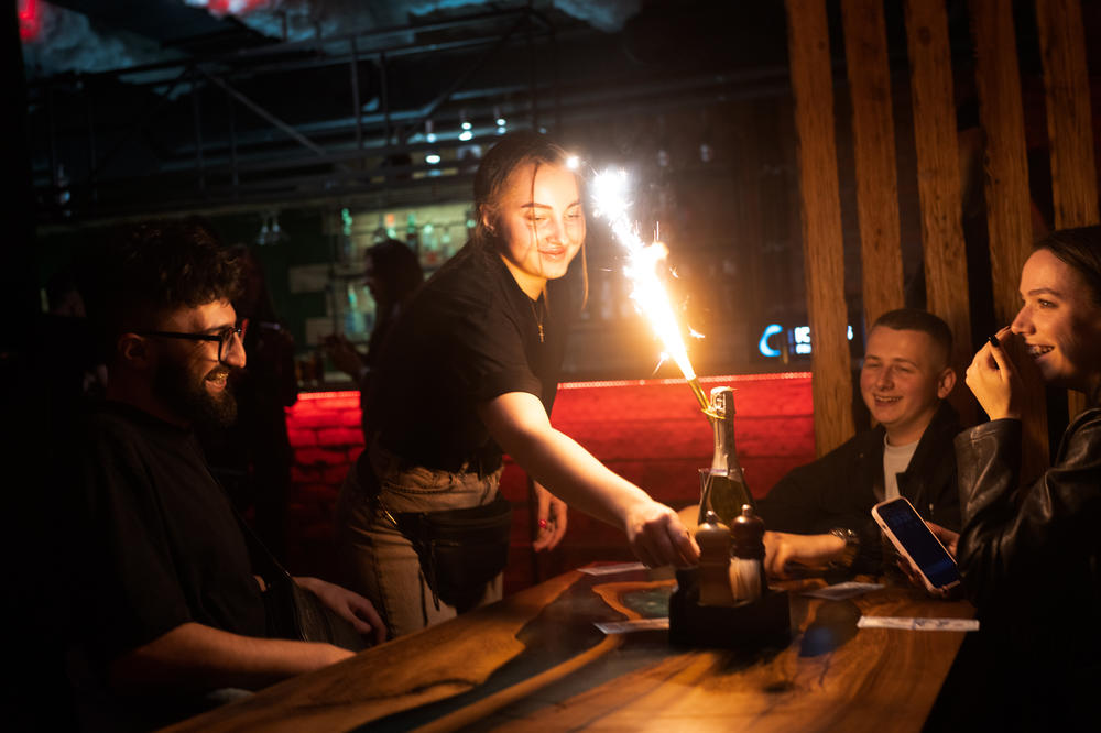 A server lights a sparkler on a bottle of champagne as she delivers it to a table.