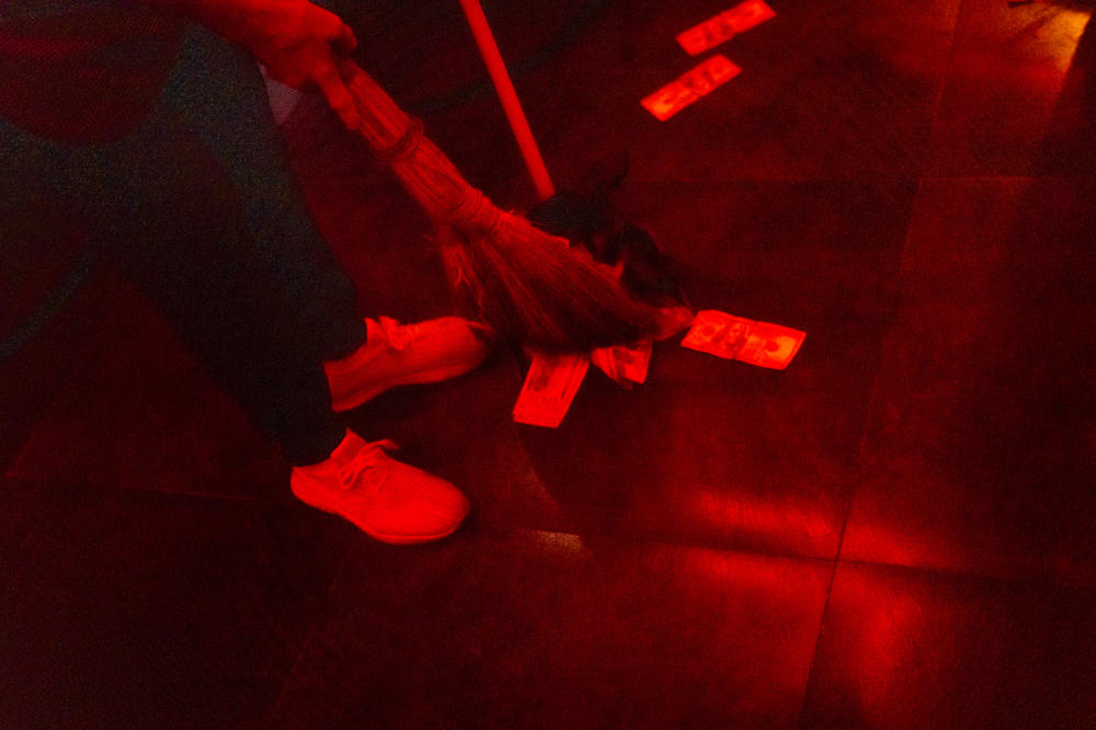 A woman sweeps up fake hundred dollar bills and broken glass after a cocktail fell on the dance floor.