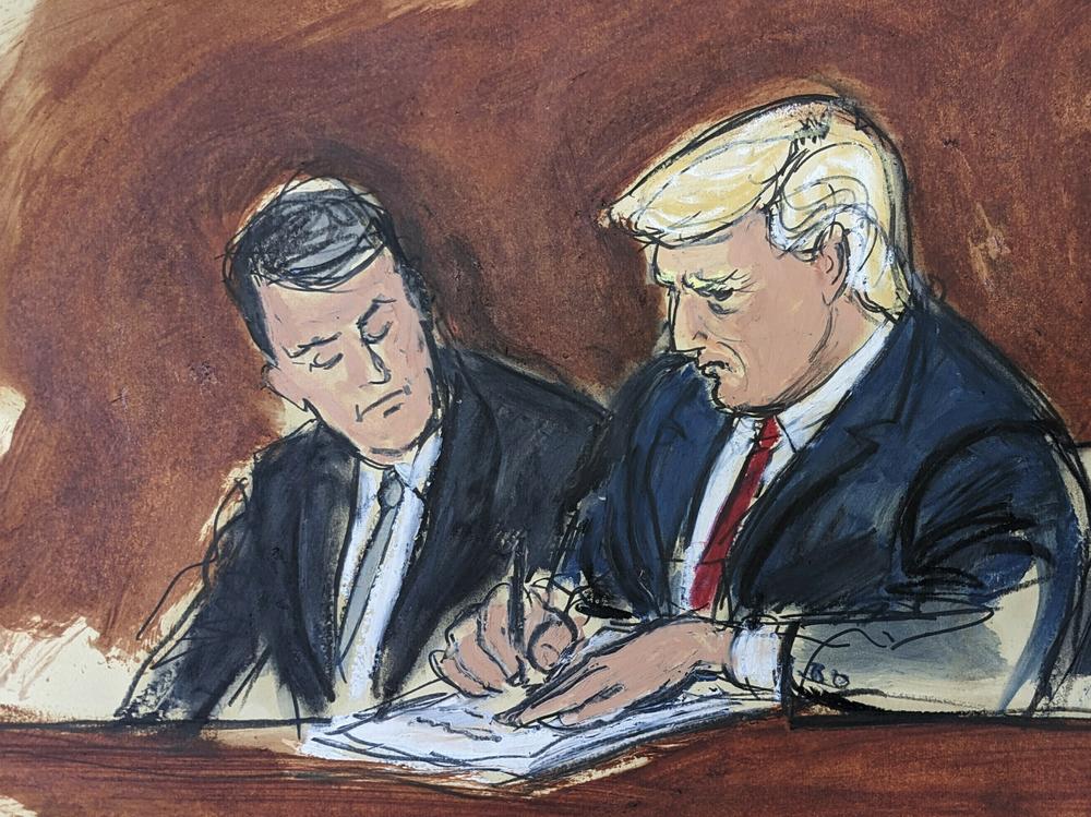 Former President Donald Trump, center, flanked by his defense attorneys, signs his bond in federal court on Tuesday in Miami. Trump plead not guilty to federal charges that he illegally kept classified documents at his Florida estate.