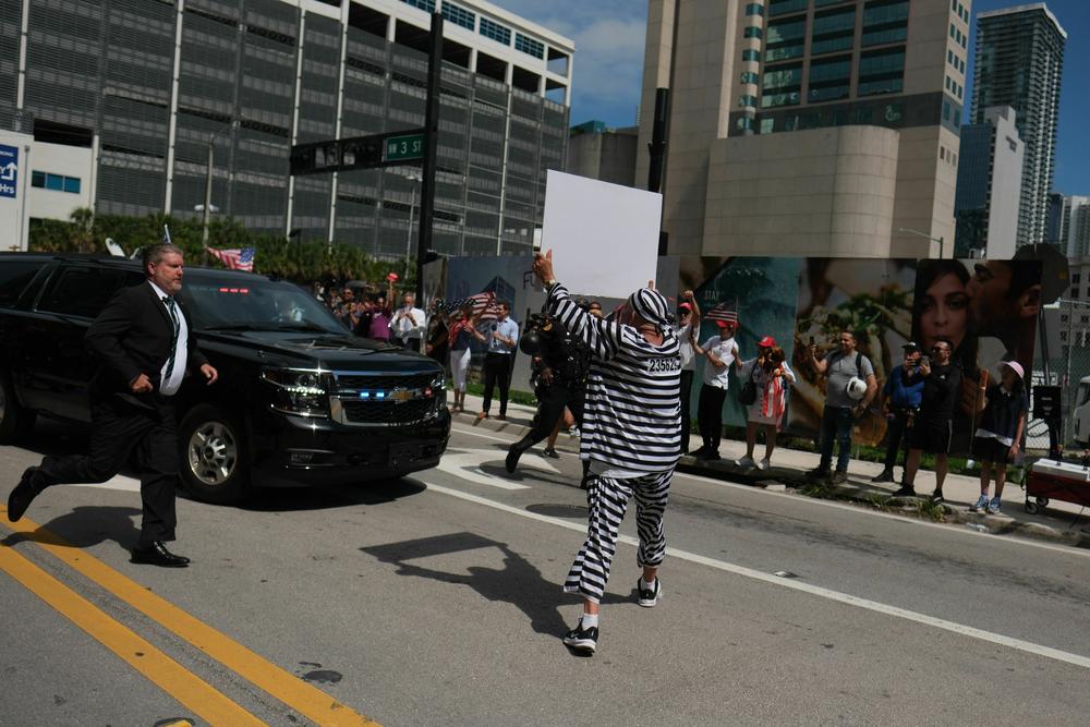 A demonstrator runs in front of a motorcade of vehicles carrying former President Trump, at Wilkie D. Ferguson Jr. United States Federal Courthouse, in Miami.