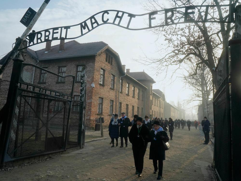 In this 2020 photo, survivors walk below a gate with the inscription 