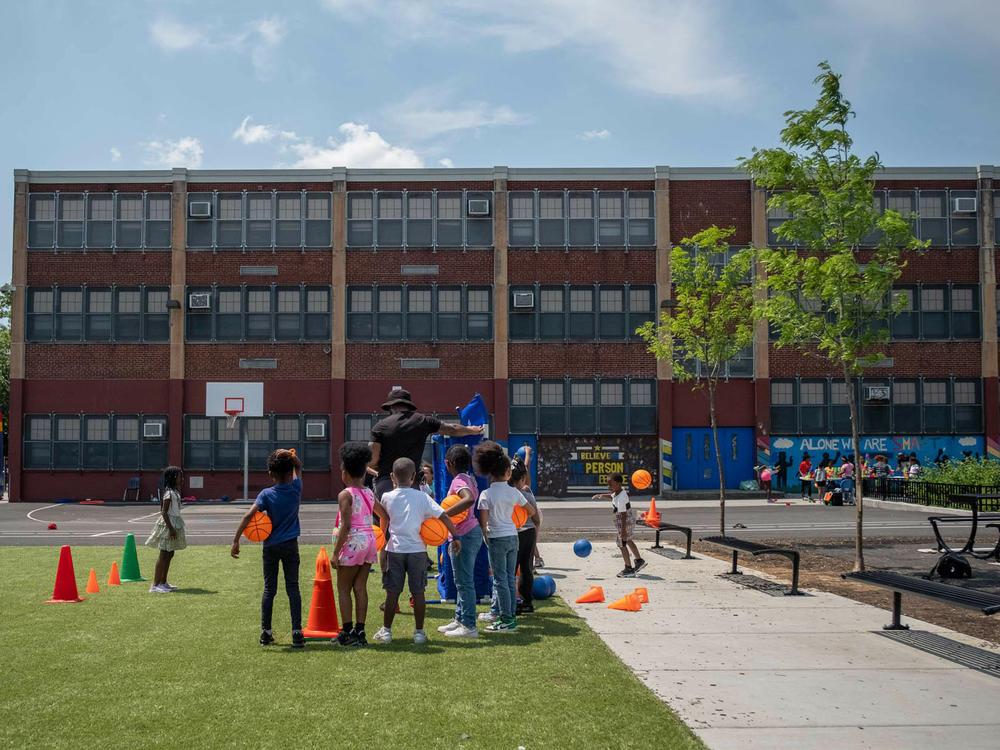 Gym teacher Delane Hart-Johnson leads kids through an exercise on Fun Day at the Add B. Anderson School. The renovated schoolyard includes a swath of green turf, benches for students to sit on and landscaped trees.