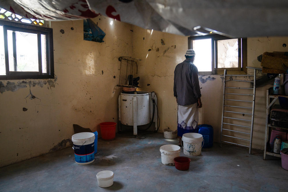 Ahmed Hameed Al Yusufi looks out the window of his building in Al Dawah. His roof has been destroyed by shelling and he's used tarps to try and cover it along with buckets across the room to catch any water that comes through.