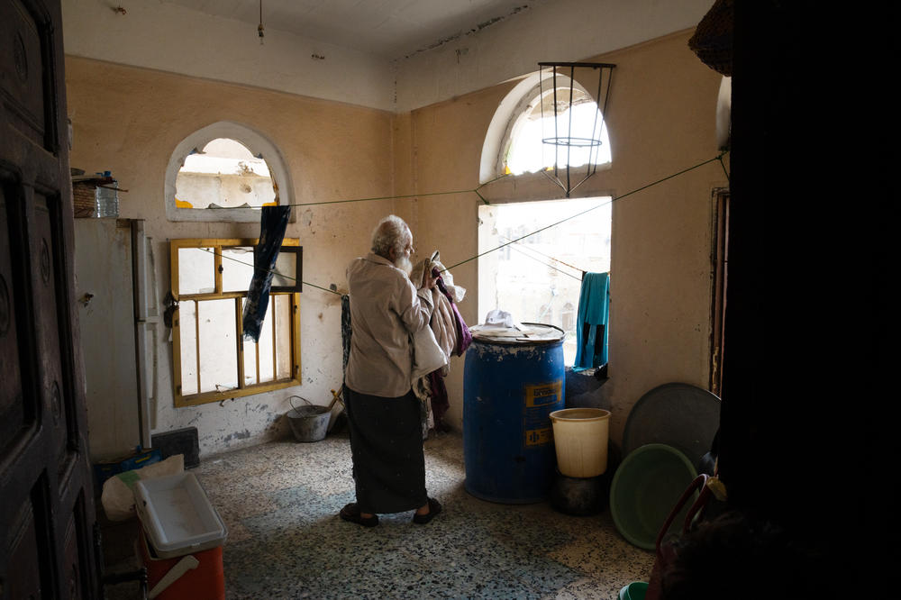 Abdullah Saif Ahmed Numan gathers laundry in his home. Nearly all of the windows are broken and he says snipers can see in from the other side of the front line.
