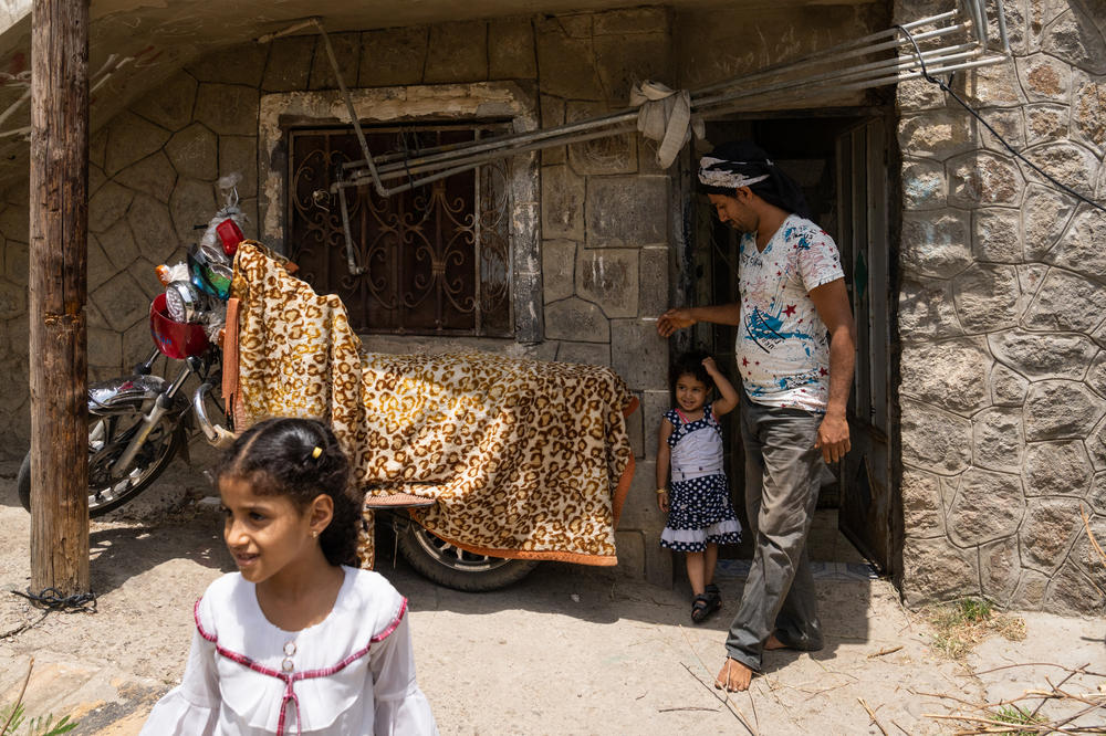 Abdullah and two of his daughters stand outside of their home in Al Dawah.