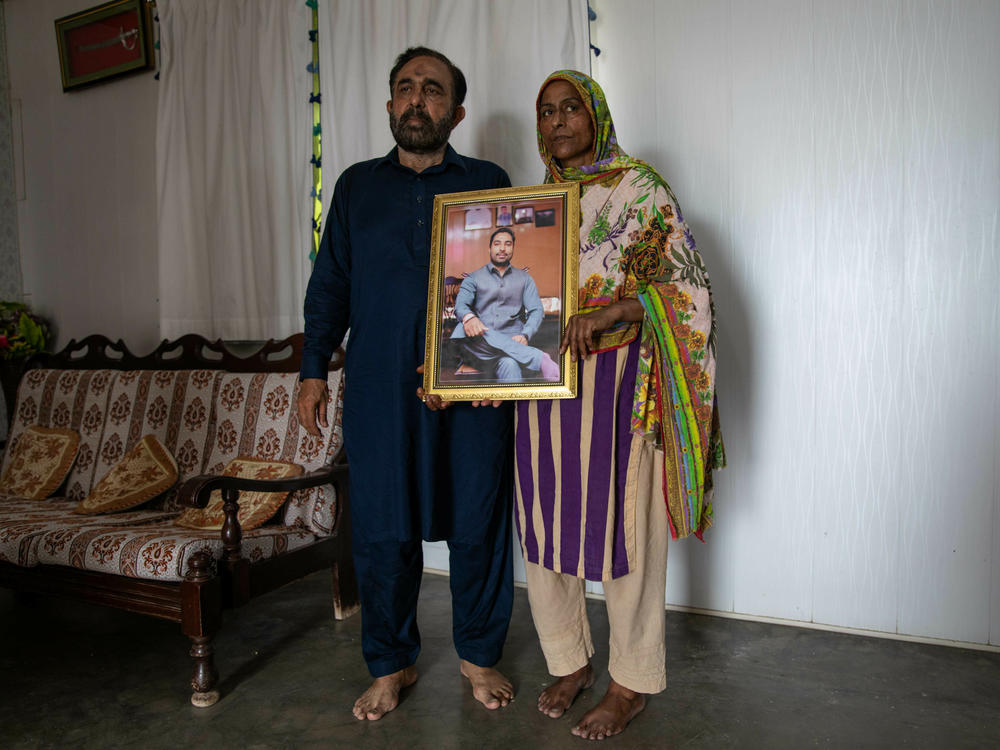 Syed Ali Raza and Rukhsana Jafri hold up a photograph of their son, Zain, who is missing after the migrant shipwreck. The family lives in Budho Kalas village, Punjab province, where Zain was a police officer. He had quit his job to start a business that wasn't profitable enough, then set off on an illegal migration to Europe for more lucrative employment.