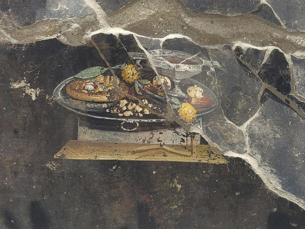 This picture provided on Tuesday, June 27, 2023, by the Pompeii Archaeological Park shows the wall of an ancient Pompeian house with a fresco depicting a table with food.