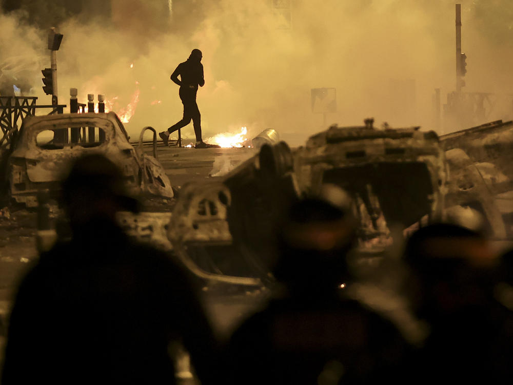 A demonstrator runs on the third night of protests sparked by the fatal police shooting of a 17-year-old driver in the Paris suburb of Nanterre, France, Friday, June 30, 2023.