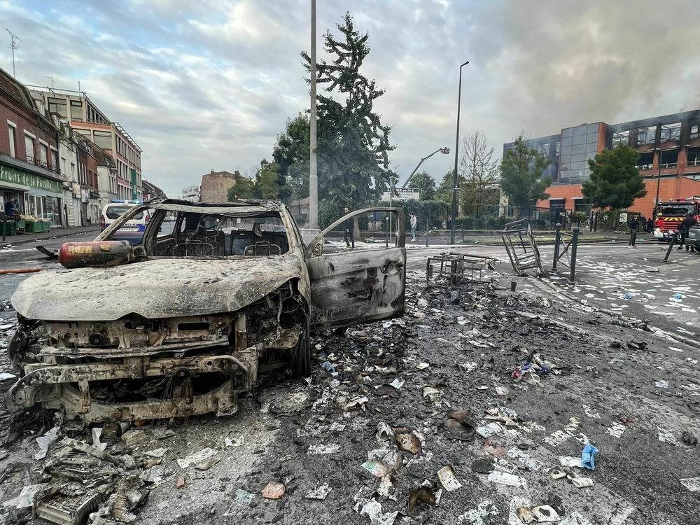 A burned-out vehicle sits near a fire-damaged building in Roubaix, France, on Friday following  protests over the death of a 17-year-old boy who was shot police in Nanterre. The building housed a data processing company for banks and insurance companies.