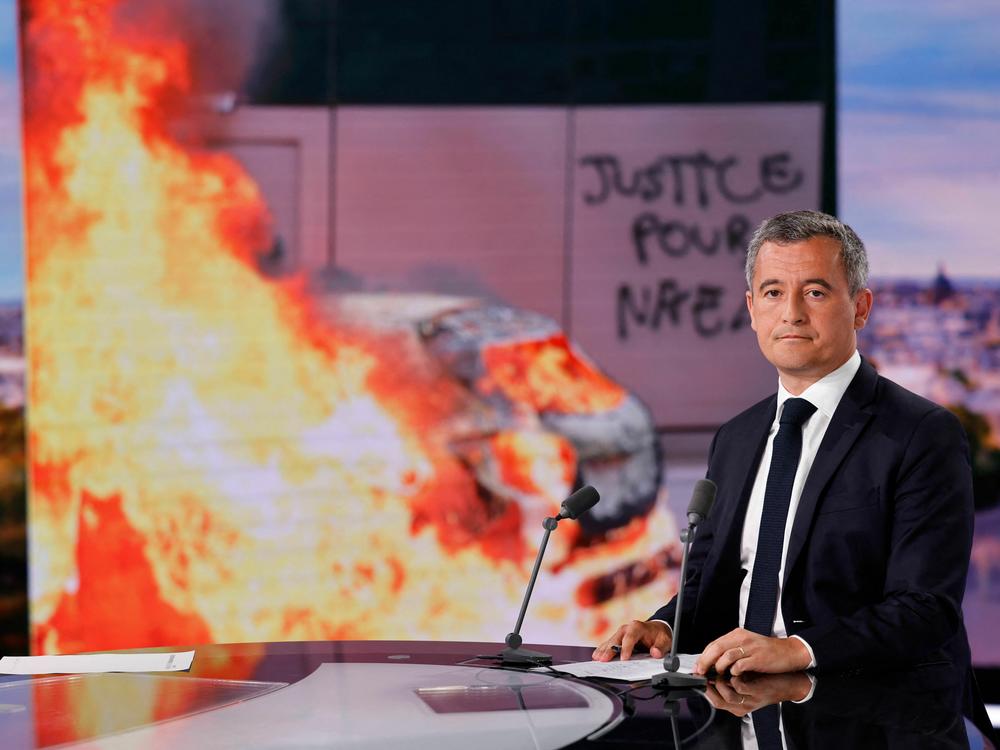 French Interior Minister Gérald Darmanin sits for an interview in the evening news broadcast of French TV channel TF1 in Boulogne-Billancourt, outside Paris, with images of major unrest on a video screen behind him.