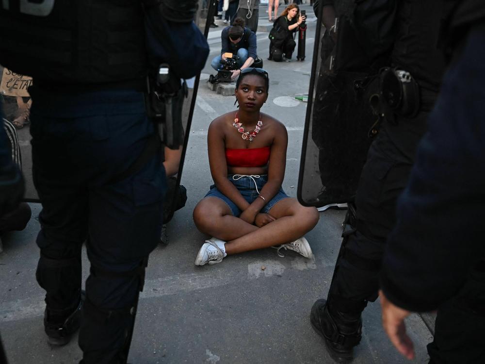 A protester sits in front of riot police during at Place de la Concorde in Paris on Friday, over the shooting of a teenage driver by French police in a Paris suburb on Tuesday.