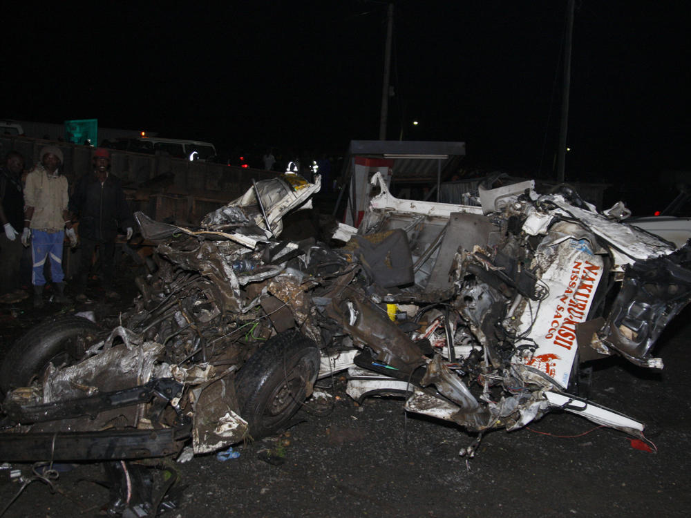 People stand near the wreckage of vehicles after a fatal accident in Londiani, Kenya, on Friday.
