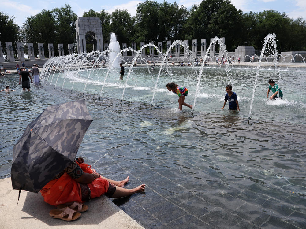 Visitors and tourists to the World War II Memorial in Washington, D.C., seek relief from the hot weather in the memorial's fountain on July 3. Due to extreme temperatures and high humidity, D.C. has declared a heat emergency, urging residents to take precautions outside and to stay hydrated.