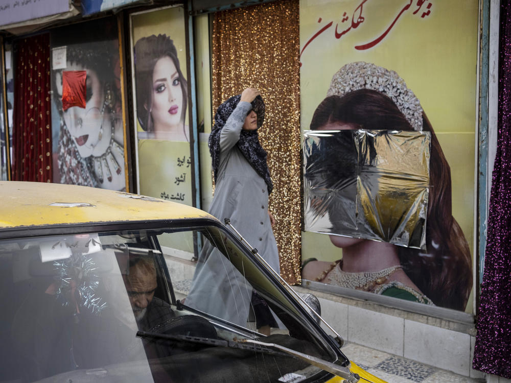 A woman walks past beauty salons with window decorations that have been defaced in Kabul, Afghanistan, Sunday, Sept. 12, 2021.