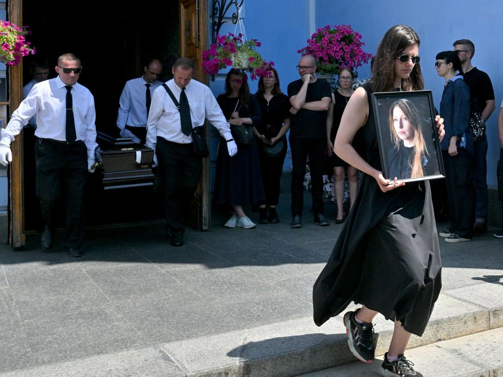 A woman holds a picture of Victoria Amelina, as pallbearers carry the writer's coffin at the end of her funeral ceremony in Mykhaylo Gold Domes in Kyiv on July 4, 2023.