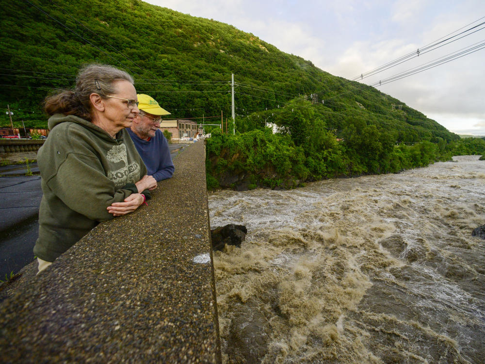 People stand on the Vilas Bridge, in Bellows Falls, Rockingham, Vt., to watch the water from the Connecticut River flow through on Monday, July 10, 2023. Heavy rain has washed out roads and forced evacuations in the Northeast, especially in Vermont and New York.