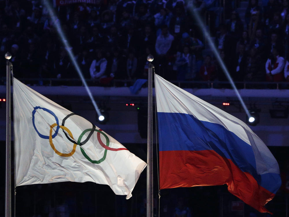 The Russian national flag, right, flies after it is hoisted next to the Olympic flag during the closing ceremony of the 2014 Winter Olympics in Sochi, Russia, Feb. 23, 2014.