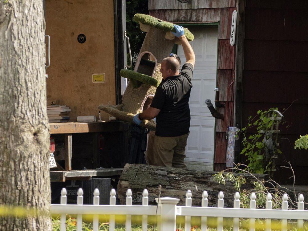 A crime laboratory officer moves a cat scratching post as law enforcement searches the home of Rex Heuermann on Saturday.