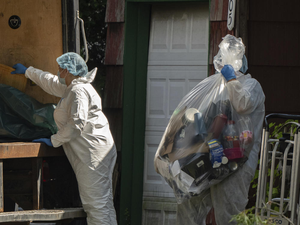A crime laboratory officer moves a plastic bag of items as law enforcement searches the home of Rex Heuermann on Saturday.
