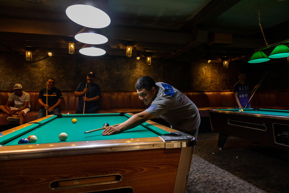 H-2A workers, including Luis Angel Lopez from Michoacán, Mexico, shoot pool after work in the lounge at the FairBridge Inn in Yakima, Wash., on June 26. The hotel's owner, First Street Investments, contracts with various farms to provide housing, meals and other services to guest workers, mostly from Mexico.