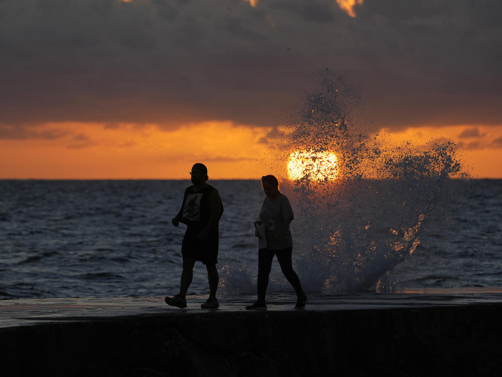 The sun rises above the Atlantic Ocean as waves crash near beachgoers walking along a jetty. Ocean temperatures averaged five degrees warmer around South Florida beginning in July.