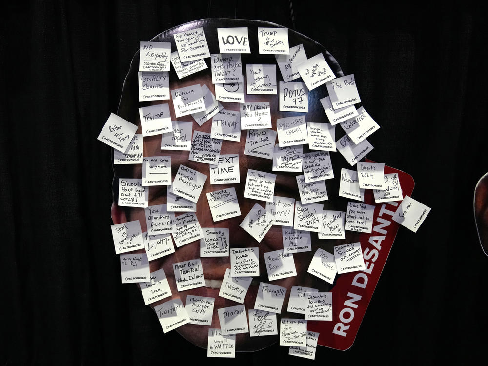 An image of Florida Gov. Ron DeSantis covered with messages written on sticky notes is displayed at an exhibit titled, 
