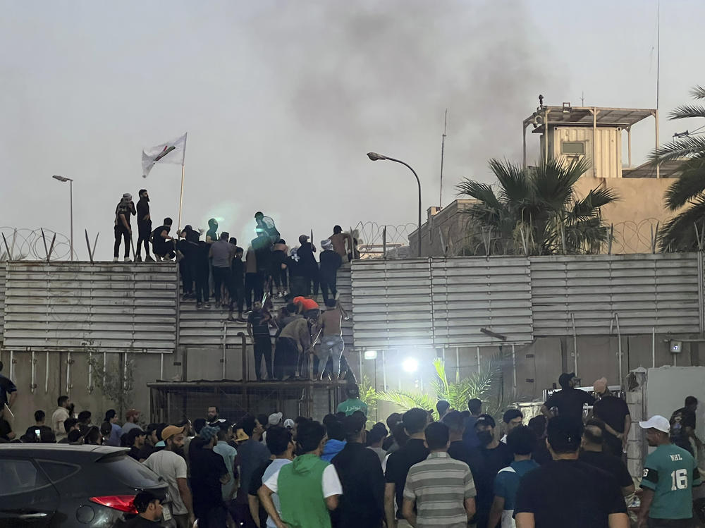 Protesters scale a wall at the Swedish Embassy in Baghdad Thursday. Protesters angered by the planned burning of a copy of the Quran stormed the Embassy early Thursday, breaking into the compound and lighting a small fire.